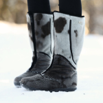 Paire de bottes hautes noires et blanches à motifs tachetés, portées dans la neige.
