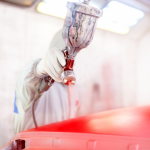 Peintre automobile appliquant de la peinture rouge au pistolet sur une carrosserie