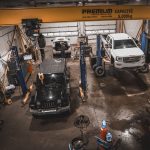 Atelier de mécanique avec plusieurs véhicules et une camionnette blanche sur un pont élévateur
