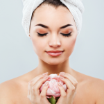 Femme portant une serviette blanche sur la tête et tenant une fleur rose entre ses mains.
