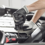 Main gantée tenant une jauge dans le compartiment moteur d’une voiture.