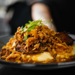 Assiette de viande garnie de morceaux croustillants et de jeunes pousses, servie sur une purée.
