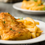 Assiette de poisson pané doré accompagné de frites et d’un quartier de citron.
