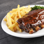 Assiette de côtes levées nappées de sauce, accompagnées de frites et de persil.