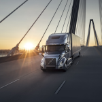 Camion Volvo gris traversant un pont à haubans au coucher du soleil.